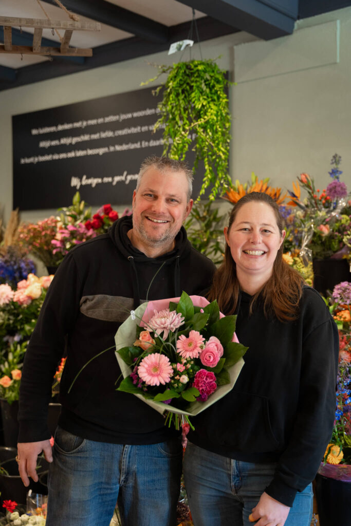 Andre en Marleen in hun eigen winkel De Bloemendijk aan de Dijkstraat in Honselersdijk. Ze houden een roze boeket bloemen in hun handen.